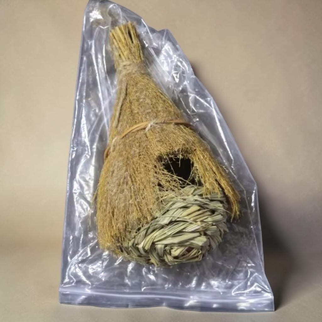 Nichoir en paille et herbe tressée toit de chaume emballé dans un sachet plastique transparent, posé sur fond beige
