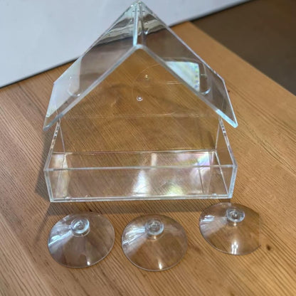 Mangeoire de fenêtre transparente à toit en pignon posée sur une table en bois, avec ses trois ventouses détachées à côté