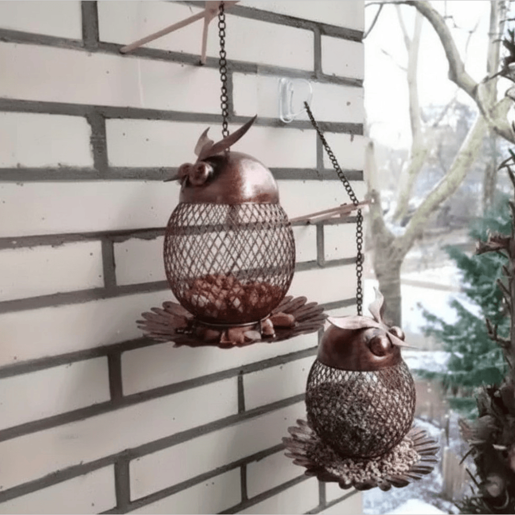 Deux mangeoires hibou en maille métallique cuivrée suspendues à un mur de briques, remplies de graines, en hiver