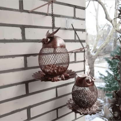 Deux mangeoires hibou en maille métallique cuivrée suspendues à un mur de briques, remplies de graines, en hiver
