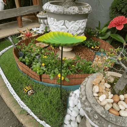 Abreuvoir à oiseaux feuille verte sur piquet installé au centre d'un massif de fleurs et plantes, avec vasque en pierre et fontaine de jardin